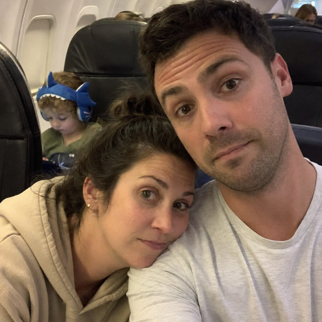 Parents relaxed on airplane with child in background